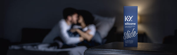 Close-up of K-Y Lubricant - Silicone box in front of a couple embracing in bed.