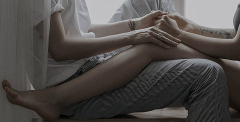 Two partners on a window sill lay their legs on each other and hold hands.